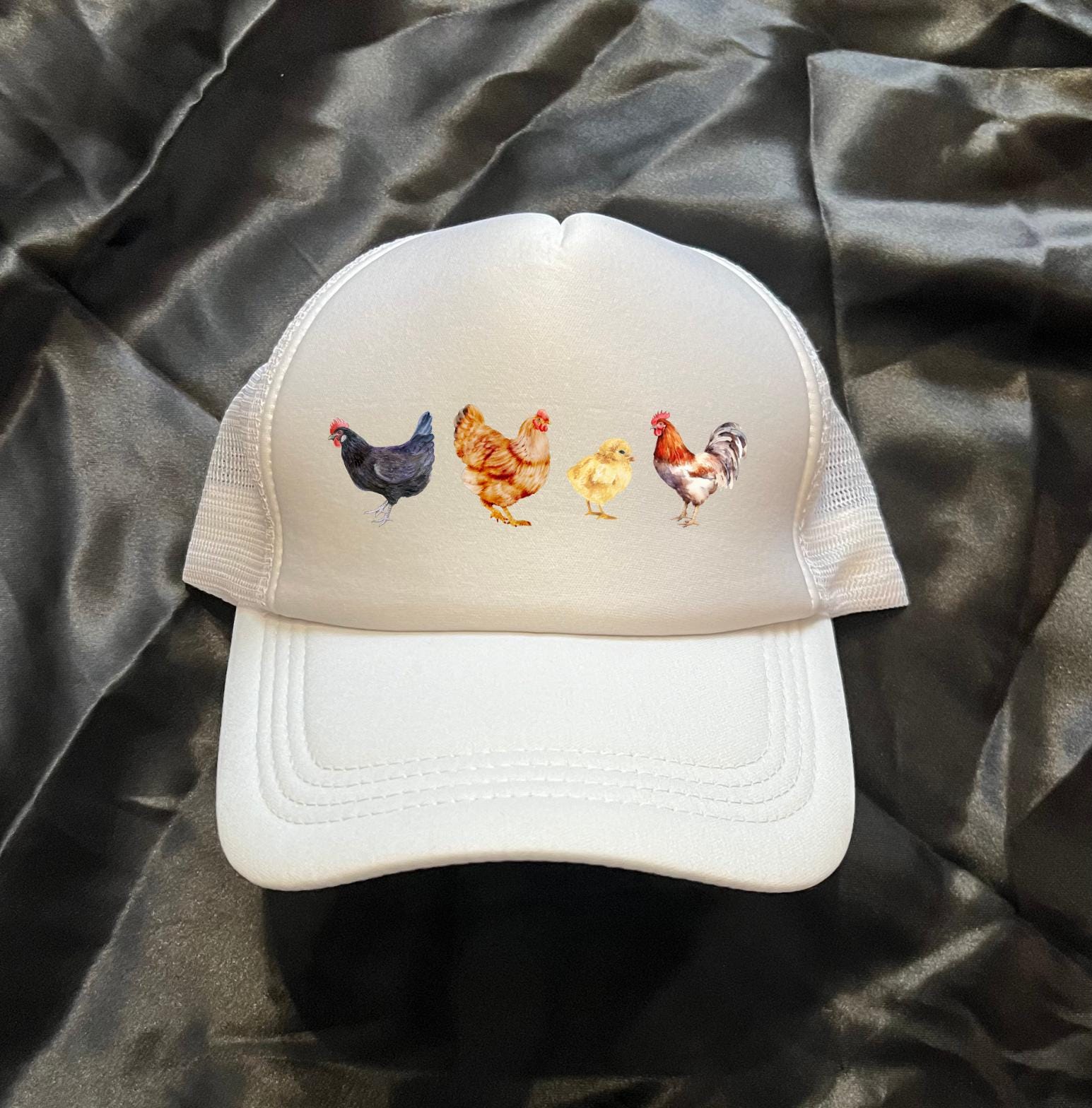 A white trucker hat is on a black background withe 4 different chicken images on the front of the hat
